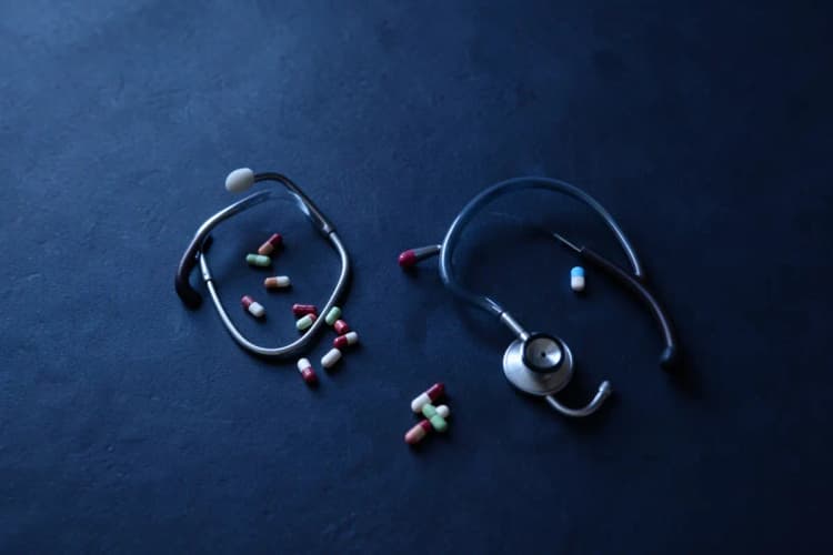 Pílulas e um estetoscópio sobre uma superfície escura, em plano médio.