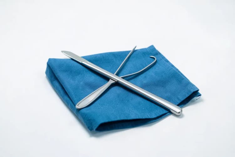Um bisturi e uma pinça sobre um pano azul, em plano detalhe.