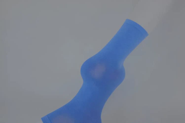 Perna com meia de compressão azul, em plano detalhe, com fundo cinza.