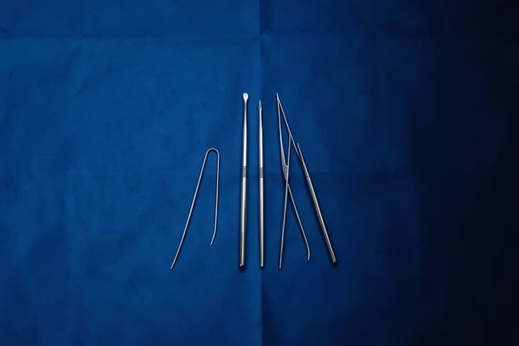 Instrumentos cirúrgicos finos e brilhantes dispostos sobre um campo cirúrgico azul, prontos para o procedimento, vista de cima, com luz de hospital clara, em um close-up.