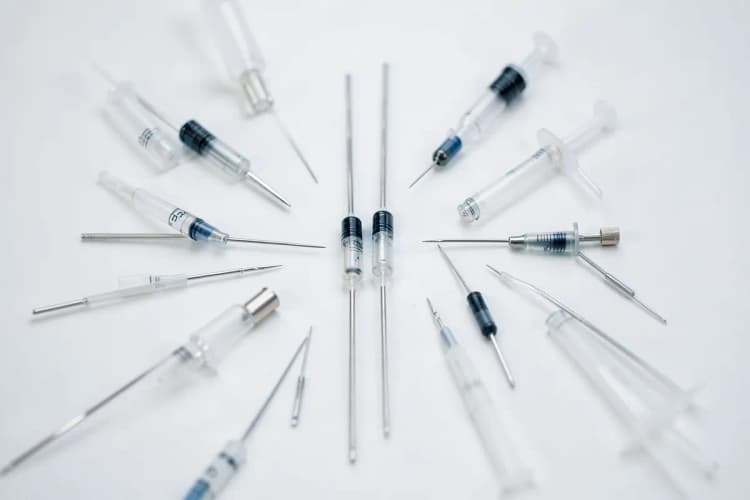 Diversos tipos de agulhas e seringas de tamanhos variados dispostos em uma superfície branca.