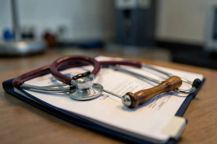 Um estetoscópio e um martelo de reflexos sobre um prontuário médico fechado