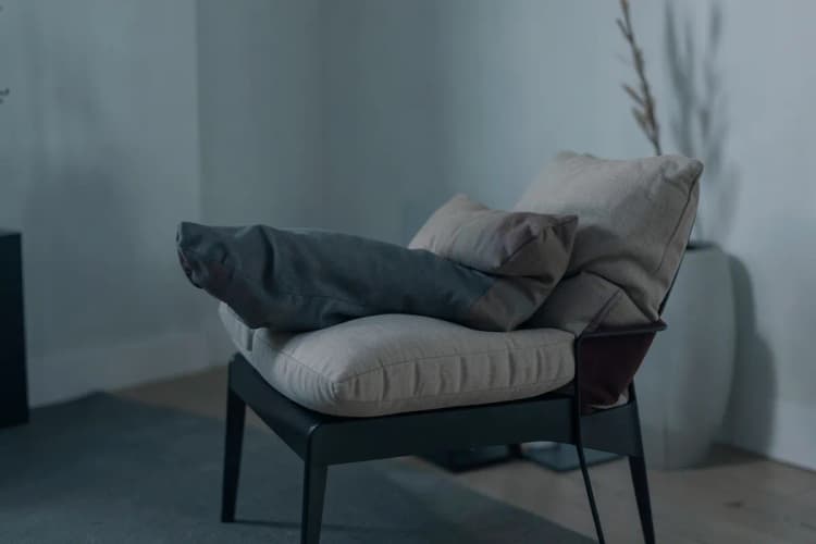 Uma pessoa sentada em uma cadeira, com as pernas elevadas e apoiadas em almofadas, em um ambiente interno com luz suave.