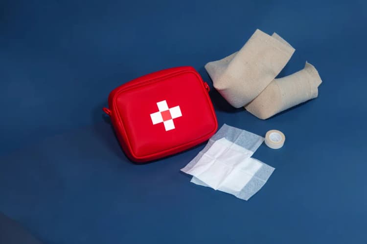 Kit de primeiros socorros com medicamentos e curativos ao lado de uma perna com faixa compressiva.