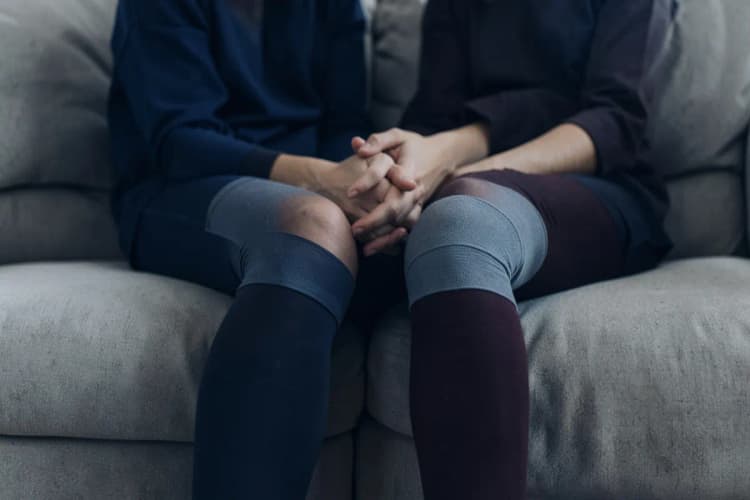 Casal de mãos dadas com meias de compressão nas pernas, sugerindo intimidade após cirurgia de varizes