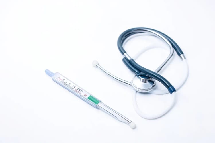 Termômetro médico e um estetoscópio sobre um fundo branco, simbolizando consulta médica após cirurgia de varizes