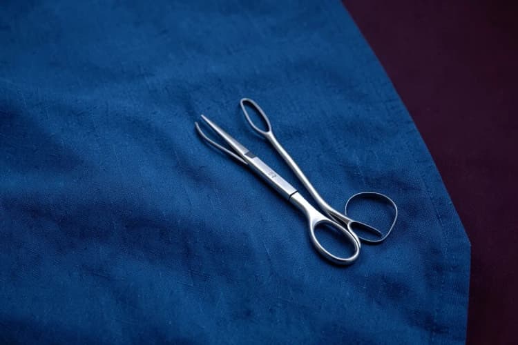 Um conjunto de instrumentos cirúrgicos, incluindo pinças e tesouras, dispostos sobre um pano azul.