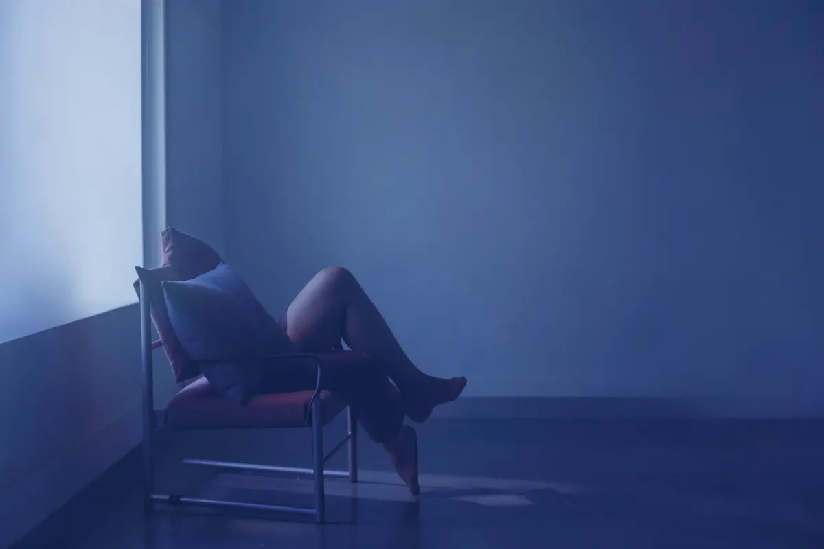 Uma pessoa sentada em uma cadeira, com as pernas elevadas e apoiadas em almofadas, em plano médio.